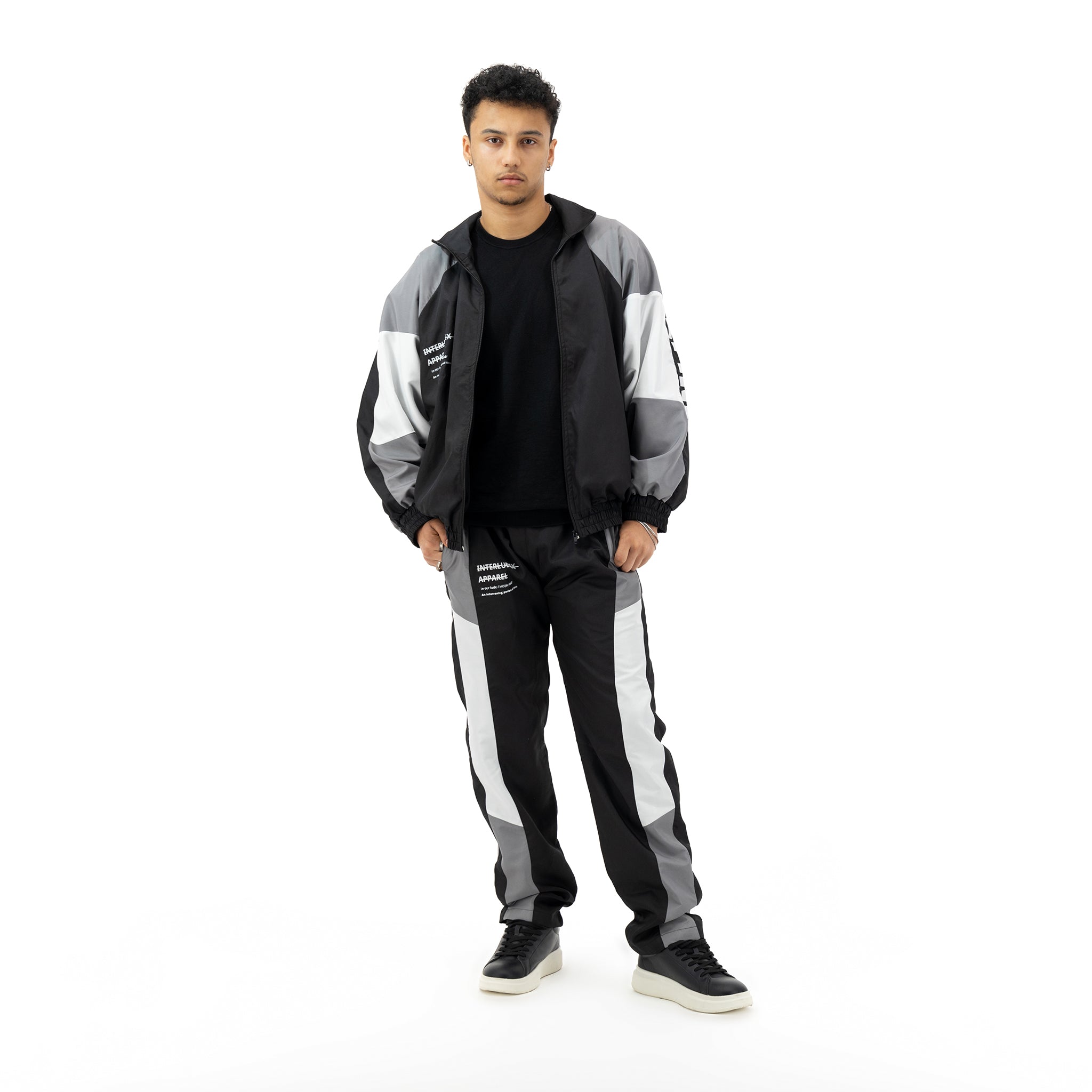 Man wearing a black, grey, and white tracksuit with a black t-shirt and black sneakers