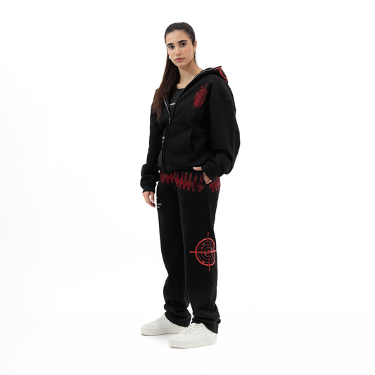 Woman wearing black zip-up hoodie and sweatpants with red graphic designs, white sneakers