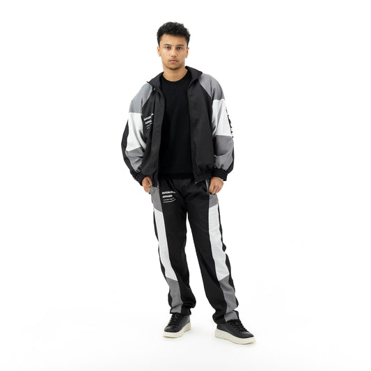 Man wearing a black, grey, and white tracksuit with a black t-shirt and black sneakers