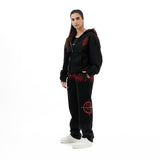 Woman wearing black zip-up hoodie and sweatpants with red graphic designs, white sneakers